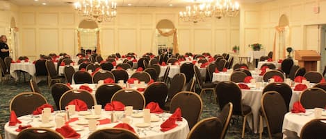 Un salón de banquetes con mesas redondas dispuestas para un evento formal, con candelabros y suelo alfombrado.