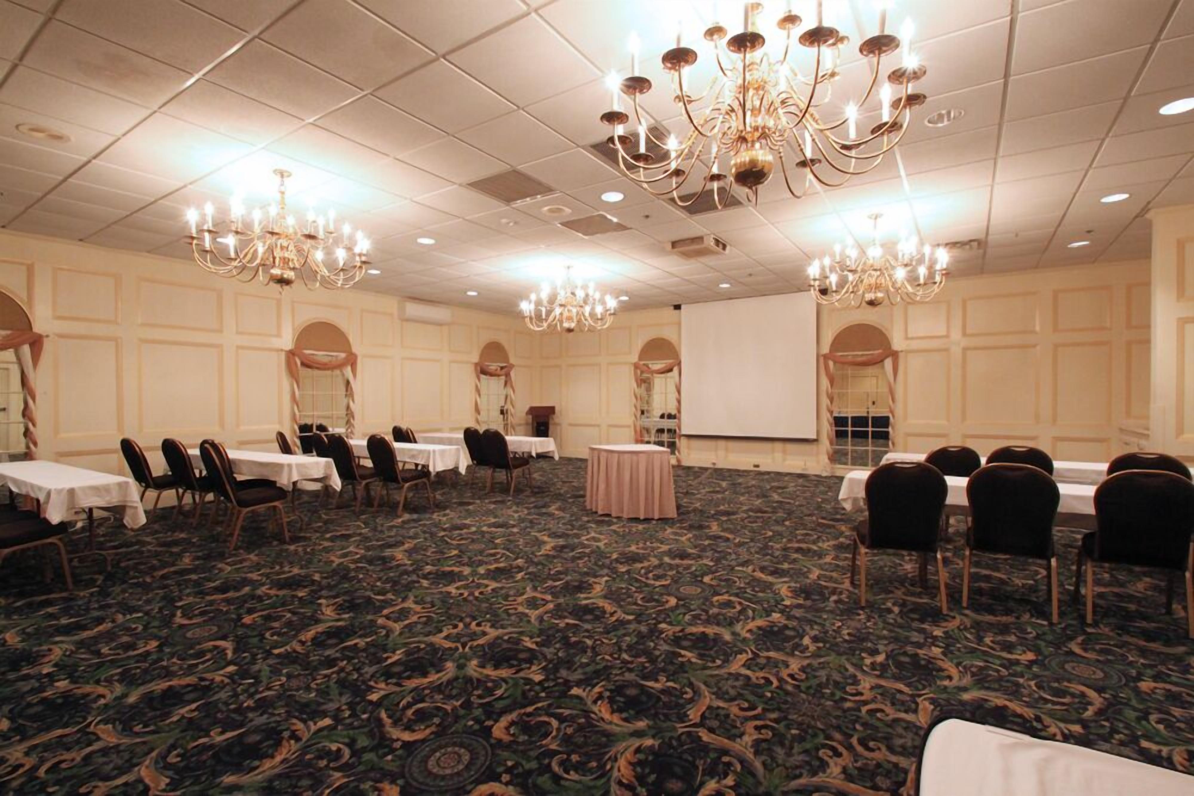 Un salón de conferencias con mesas, sillas, candelabros y una pantalla de proyector.