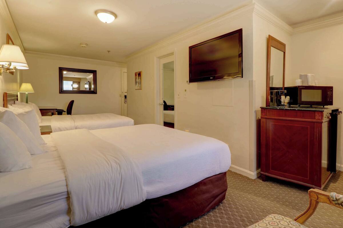 A hotel room with two beds, a television, a microwave, and a wooden cabinet.