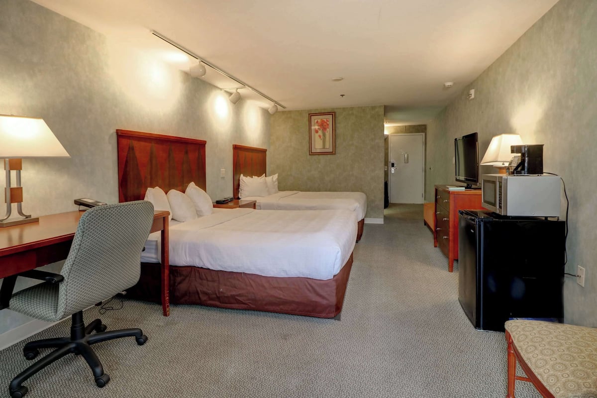 A hotel room with two beds, a desk, a chair, a TV, and a minibar.