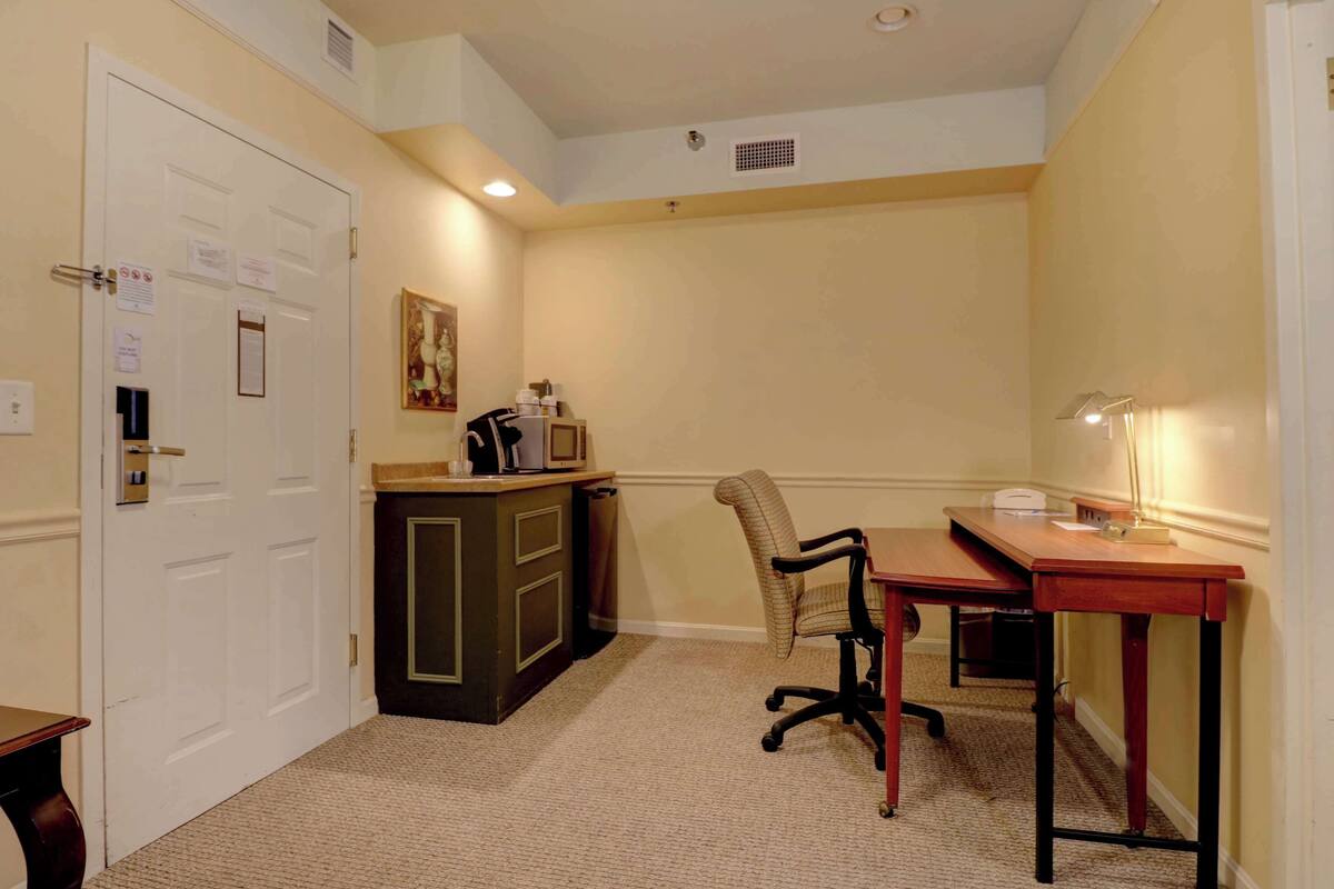 A small, well-lit room with a desk, chair, and kitchenette.