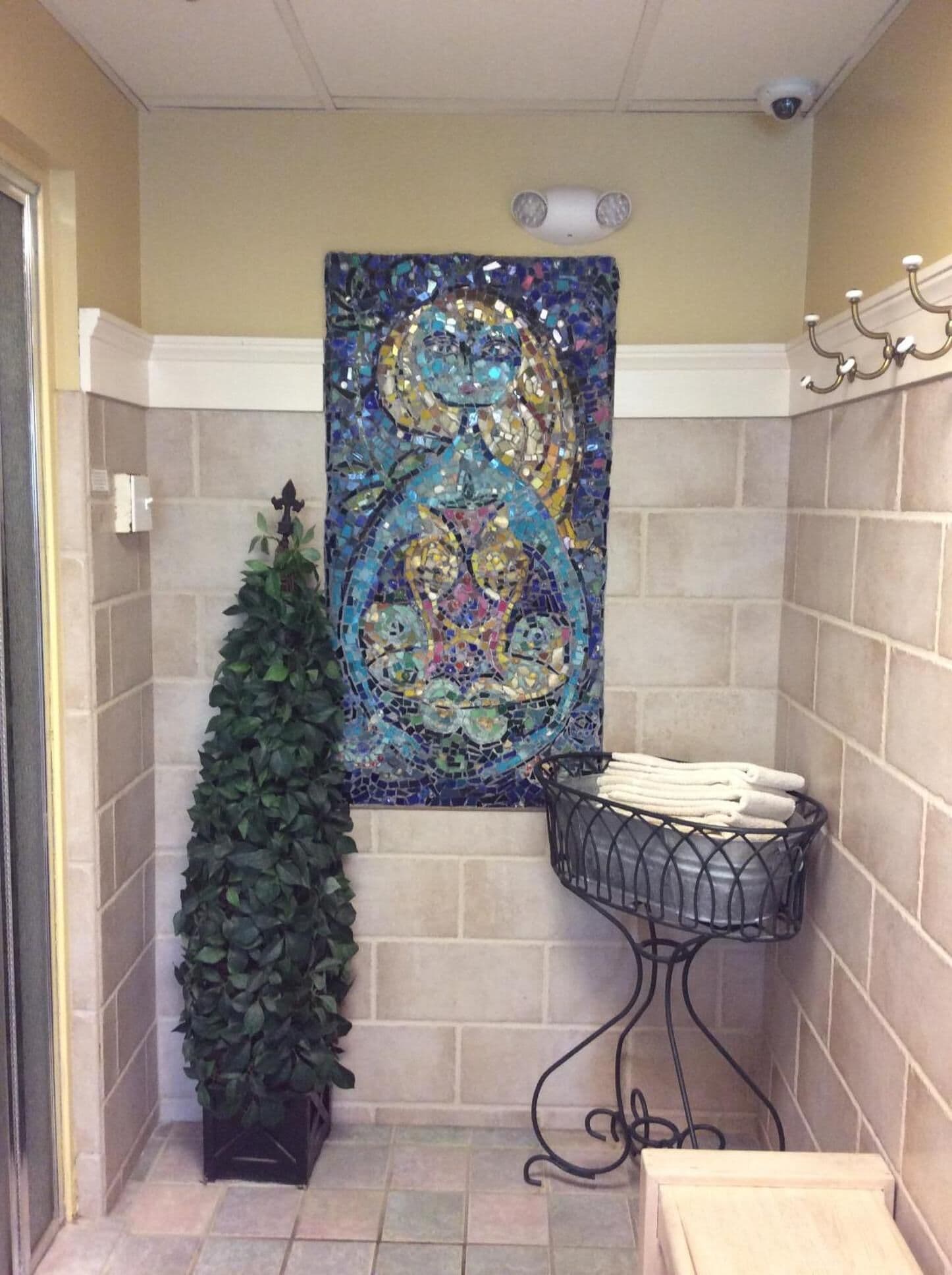 A bathroom with a mosaic artwork on the wall, a potted plant, and a towel rack.