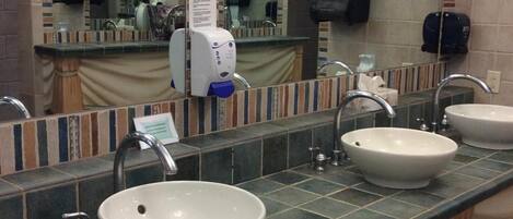 A bathroom with three sinks, a hand dryer, and a soap dispenser.