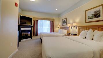 A hotel room with two beds, a television, a fireplace, and a painting on the wall.