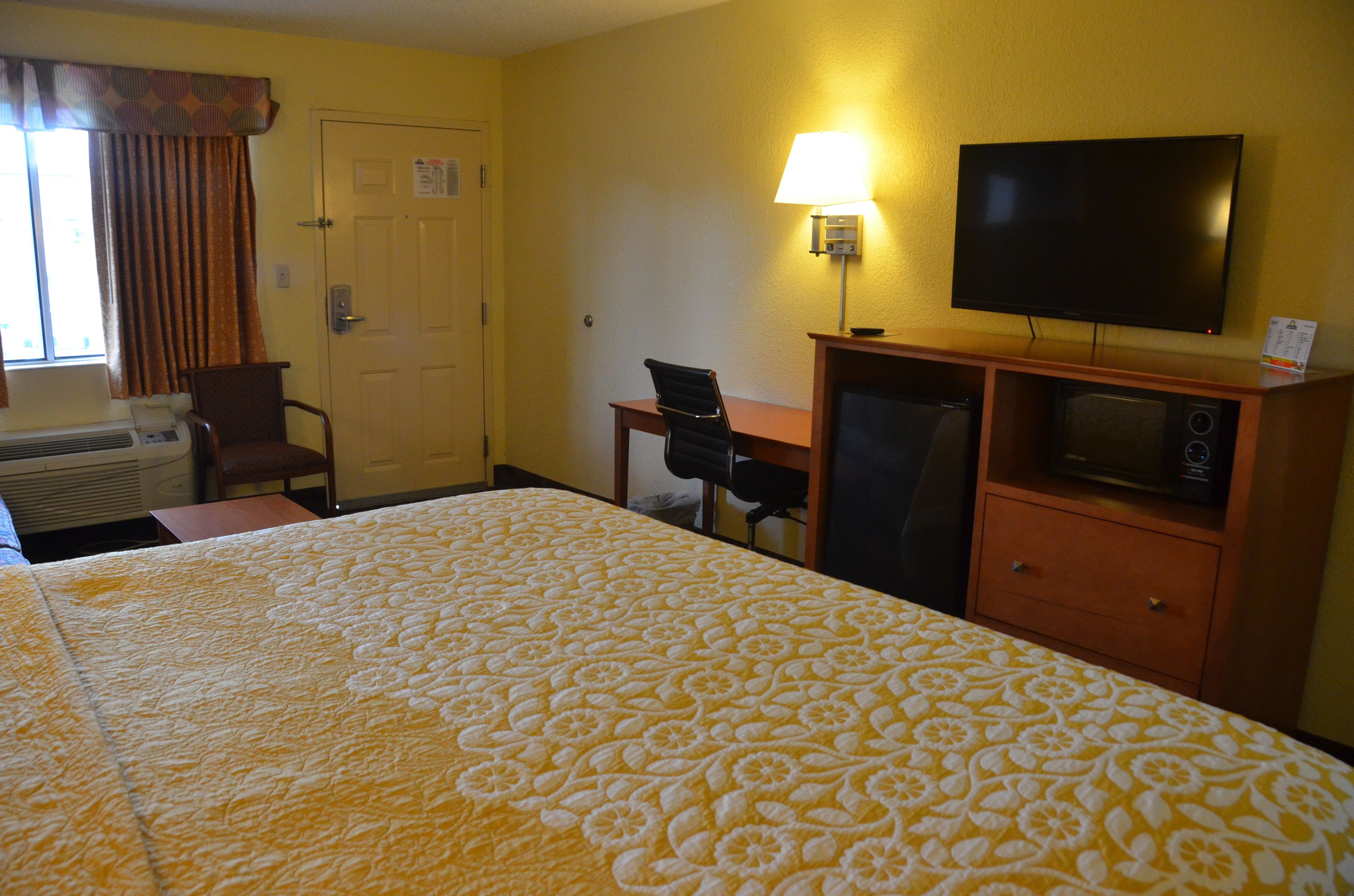 A hotel room with a bed, a desk, a chair, a television, and a microwave.