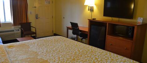 A hotel room with a bed, a desk, a chair, a television, and a microwave.