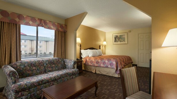 A hotel room with a floral sofa, a wooden table, a striped chair, a bed with patterned bedding, and two bedside lamps. - Days Inn by Wyndham Nashville Airport (Nashville)