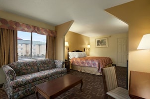 A hotel room with a floral sofa, a wooden table, a striped chair, a bed with patterned bedding, and two bedside lamps.