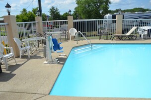 A swimming pool with a white fence, lounge chairs, and a covered area with tables and chairs.