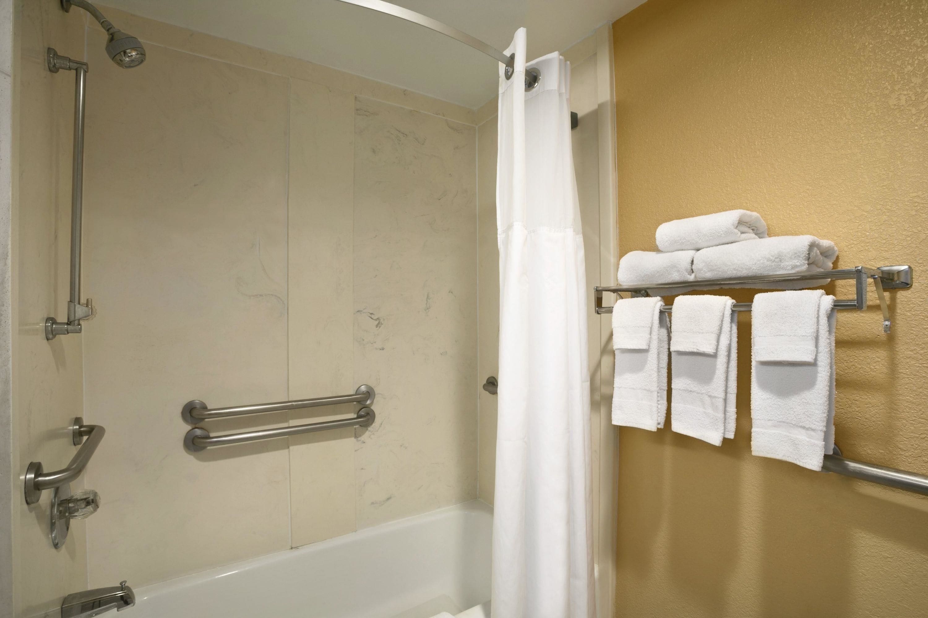A bathroom with a bathtub, a shower with a glass door, and a towel rack with folded towels.