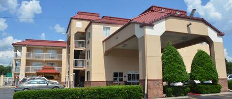A multi-story hotel with a red roof, a covered entrance, and a parking lot.