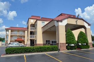 A multi-story hotel with a red roof, a covered entrance, and a parking lot.