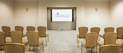 A conference room with rows of chairs facing a projection screen displaying 'Ocean Breeze Inn Vero Beach FL'.