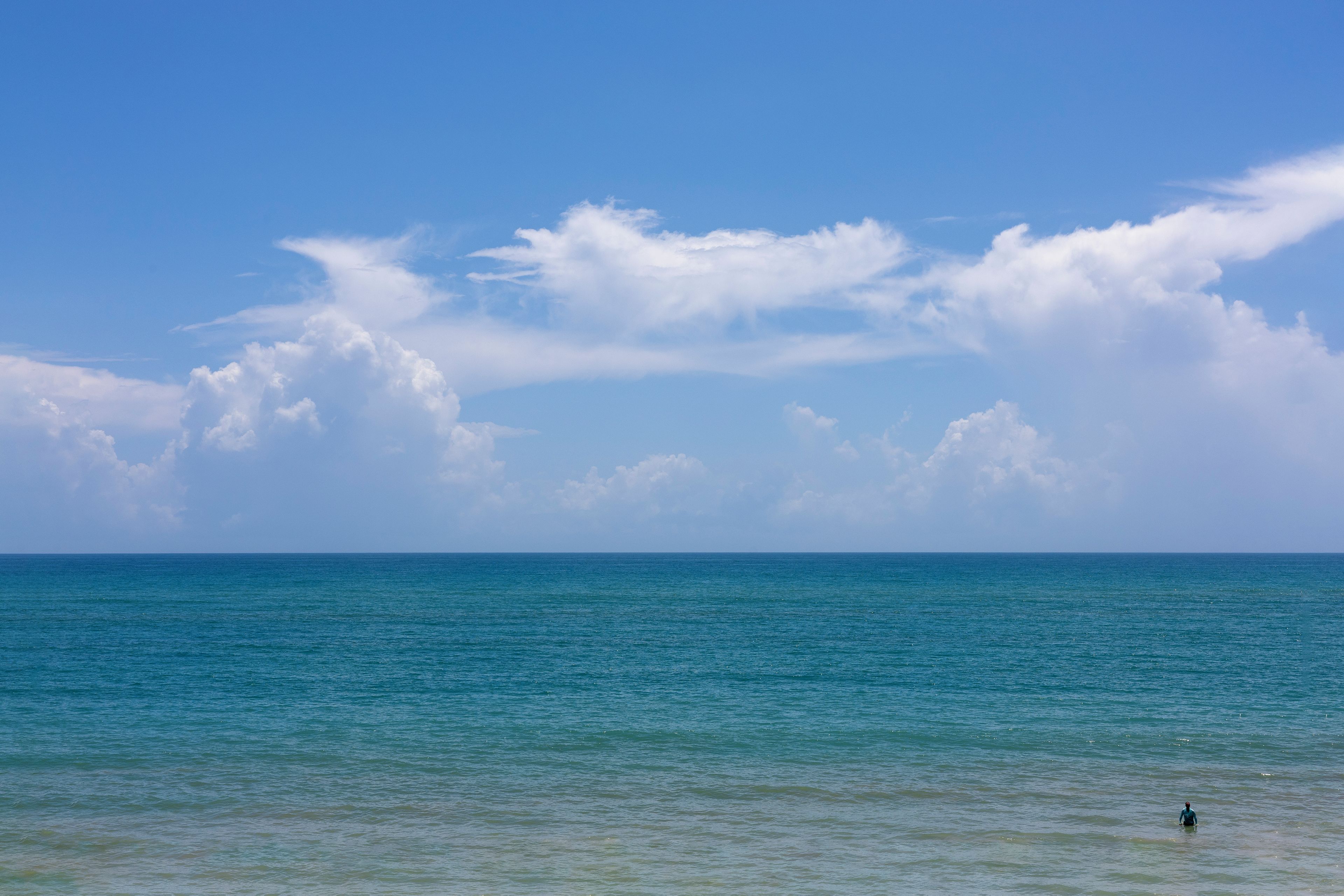 A clear blue sky with clouds over a calm sea.