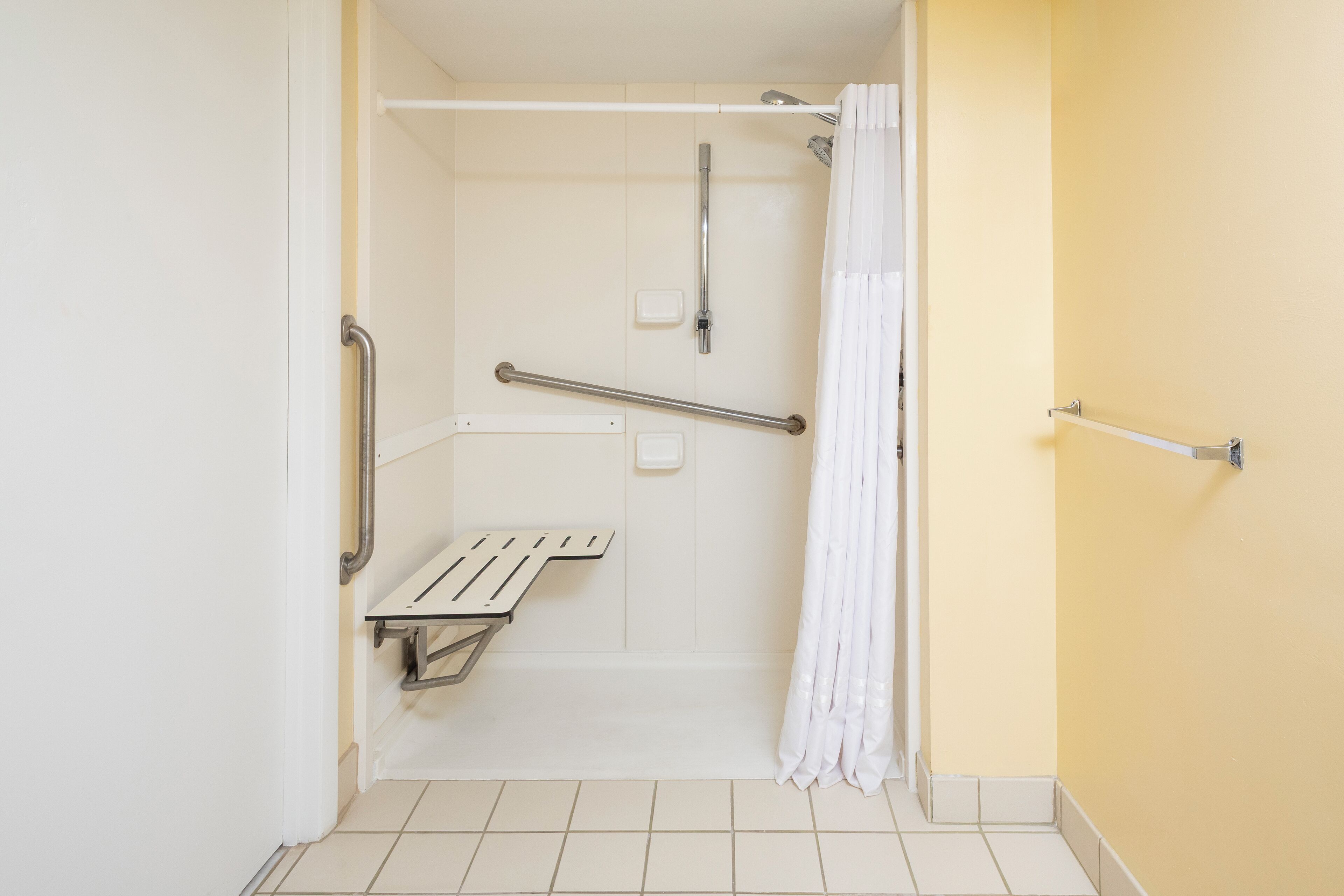A bathroom with a shower, grab bars, and a white towel rack.