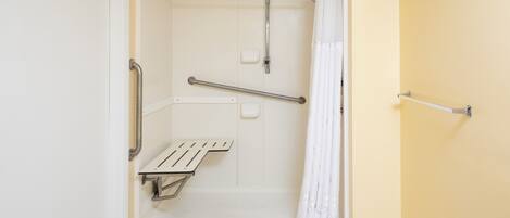 A bathroom with a shower, grab bars, and a white towel rack.