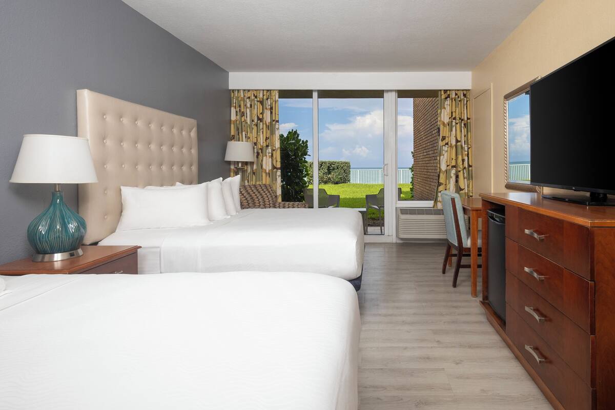 A hotel room with two beds, a TV, a desk, and a balcony with a view.