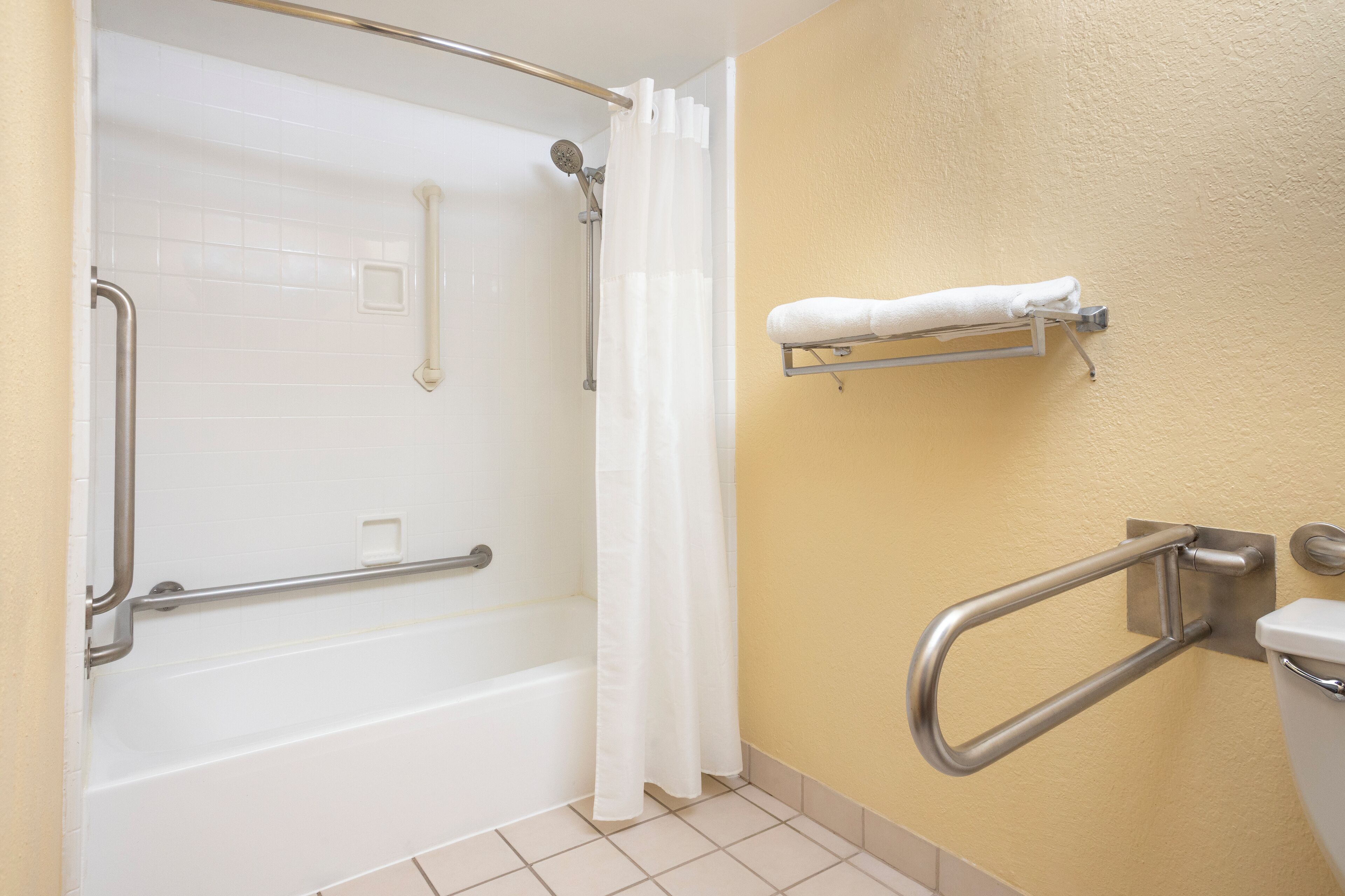 A bathroom with a white bathtub, a shower with a grab bar, a white towel rack, and a toilet with a grab bar.
