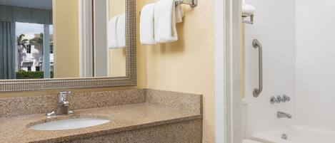 A bathroom with a granite countertop, a sink, a mirror, a shower, and a toilet.