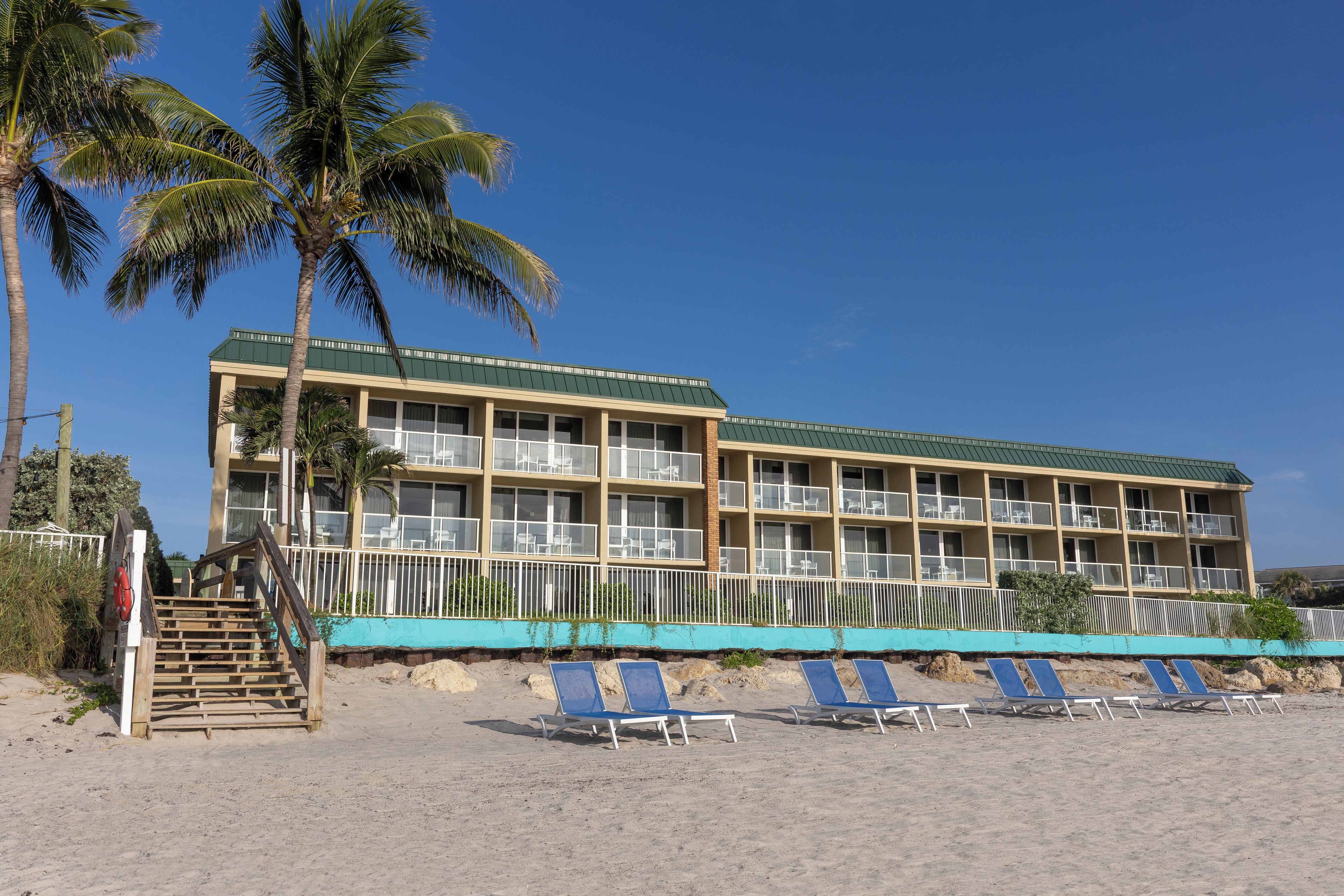A hotel with a green roof, multiple balconies, and a beachside location with lounge chairs.
