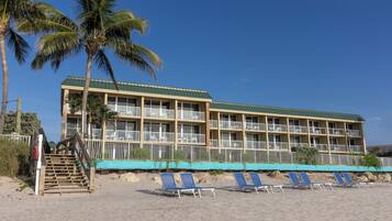 A hotel with a green roof, multiple balconies, and a beachside location with lounge chairs.