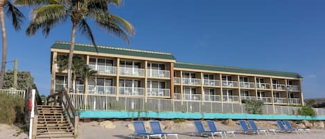 A hotel with a green roof, multiple balconies, and a beachside location with lounge chairs.