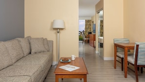 A living room with a sofa, a coffee table with a magazine, a lamp, and a dining area with chairs and a table. - Ocean Breeze Inn Vero Beach (Vero Beach)