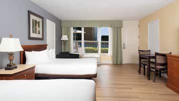 Habitación de hotel con dos camas, un escritorio y una silla. Hay una ventana con cortinas, una lámpara en el escritorio y un cuadro en la pared.