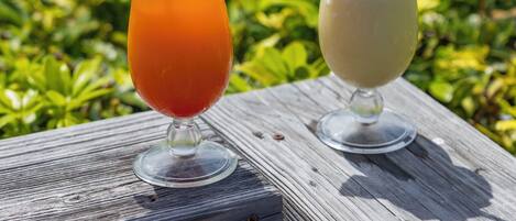 Two cocktails on a wooden table by a pool with a clear blue sky in the background.