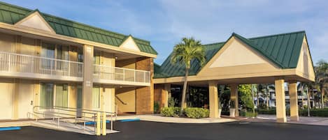 A hotel with a covered outdoor area, a parking lot, and a building with a green roof.