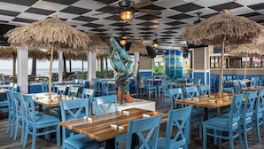 A restaurant with blue chairs and wooden tables, thatched umbrellas, and a view of the ocean. - Ocean Breeze Inn Vero Beach (Vero Beach)