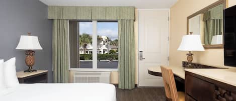 A hotel room with a bed, a desk, a chair, a dresser, a mirror, and a window with curtains.