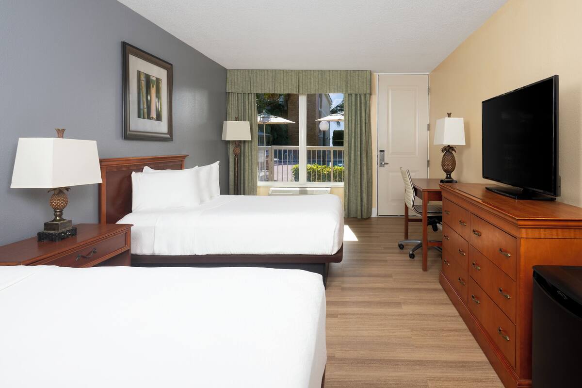 A hotel room with two beds, a television, a desk, and a window with curtains.