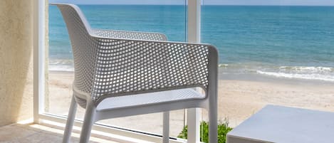 Un balcón con una silla y una mesa blancos, con vista a una playa y al océano.