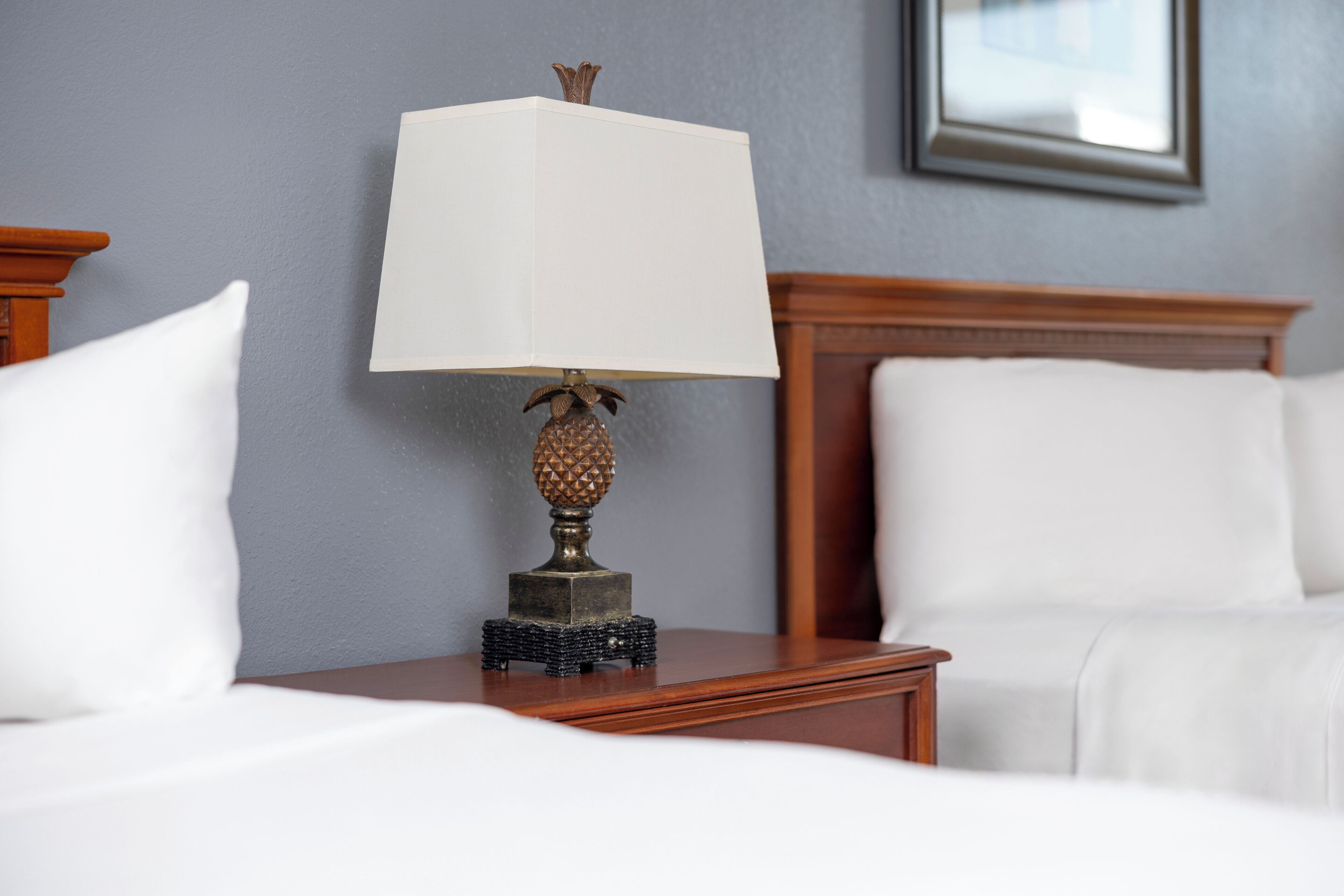 A neatly made bed with white linens, a wooden nightstand with a lamp, and a framed picture on the wall.
