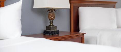 Ein ordentlich bezogenes Bett mit weißen Leinen, ein Nachttisch aus Holz mit einer Lampe und ein gerahmtes Bild an der Wand.