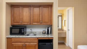 A compact kitchen with wooden cabinets, a microwave, a coffee maker, and a dishwasher.