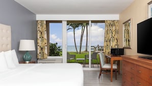 A hotel room with a large bed, a desk with a chair, a TV, and a view of the ocean through a sliding door. - Ocean Breeze Inn Vero Beach (Vero Beach)