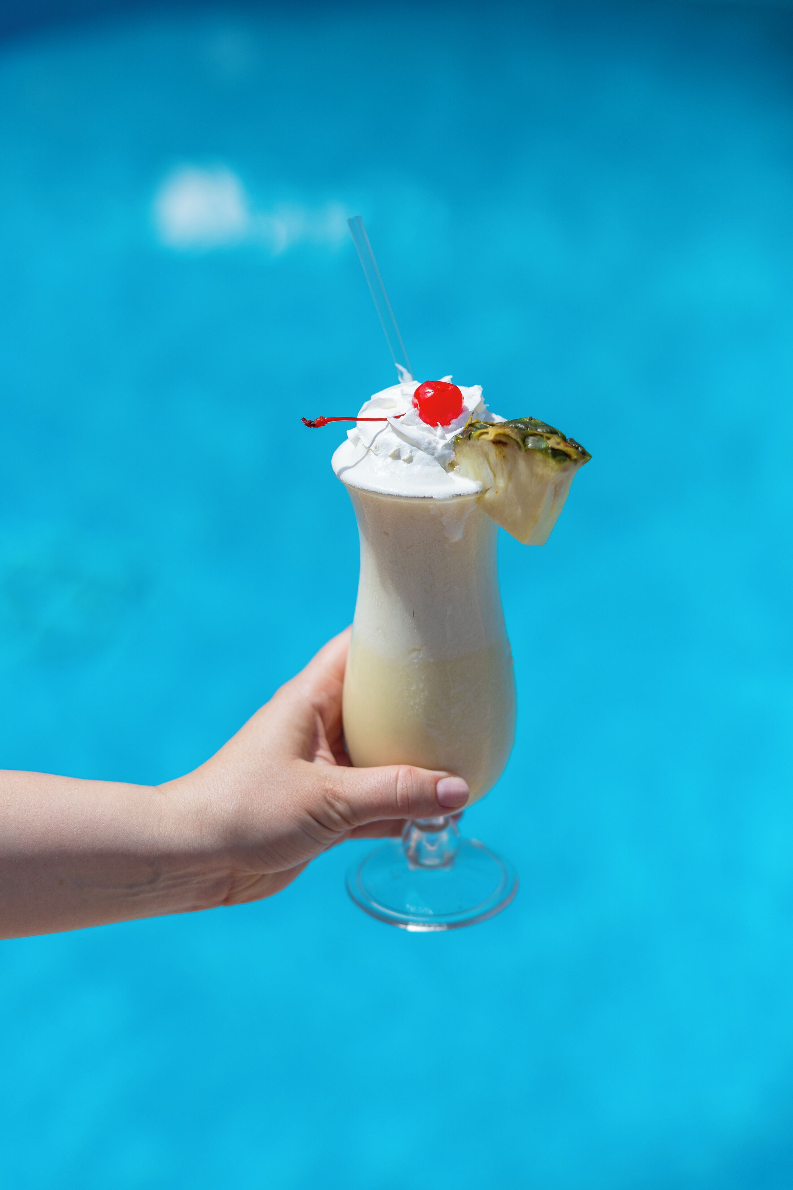 A hand holding a milkshake with whipped cream and a cherry on top, against a blue background.