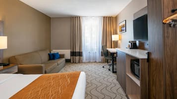A hotel room with a bed, a sofa, a desk, a TV, and a microwave.
