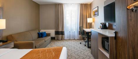 Een hotelkamer met een bed, een bank, een bureau, een televisie en een magnetron.