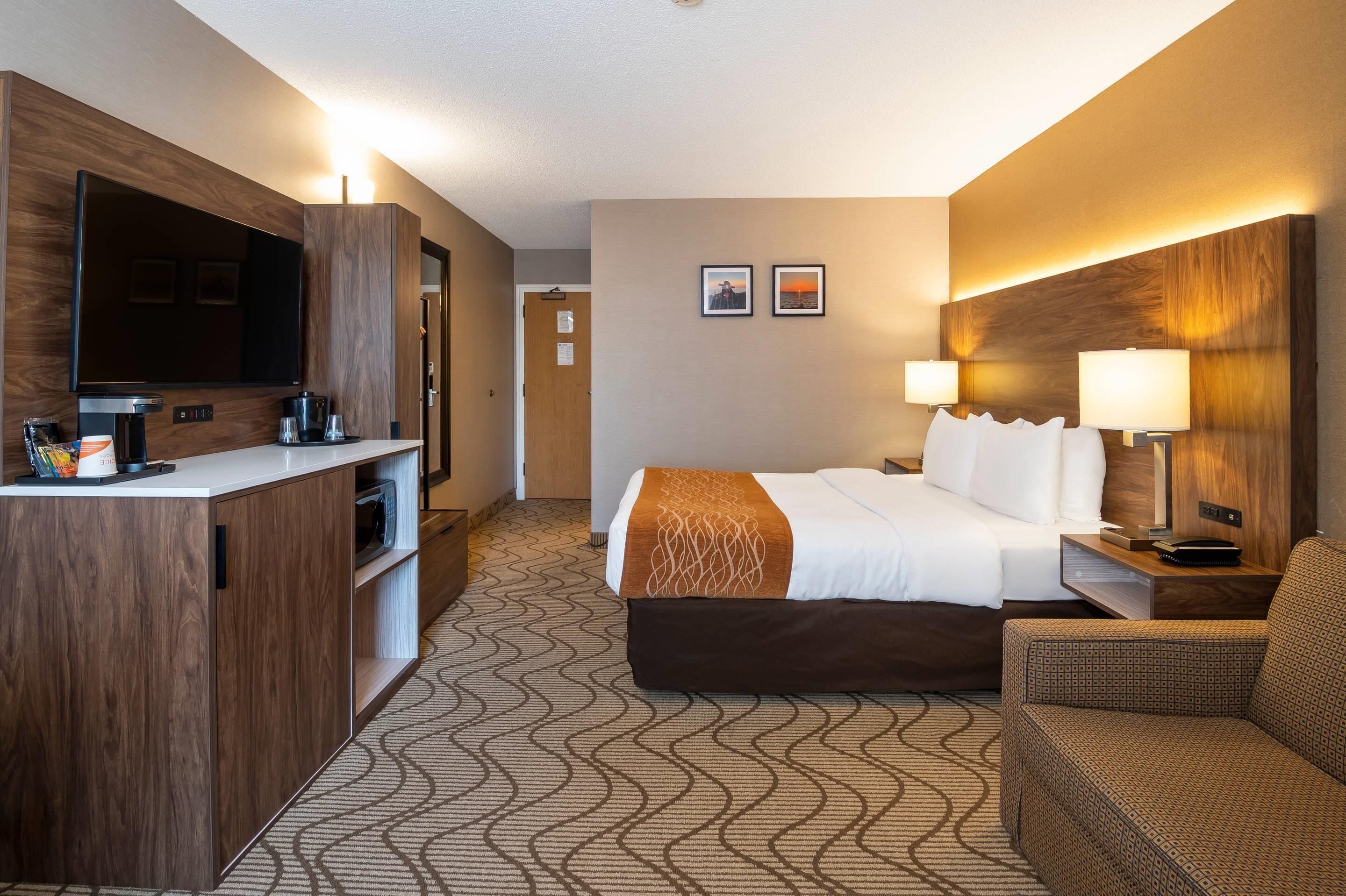 A hotel room with a bed, a desk with a flat-screen TV, a coffee maker, and a chair.