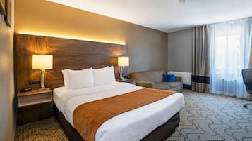 Hotelkamer met een groot bed, twee bedlampen, een bureau, een stoel en uitzicht op het landschap door een raam.