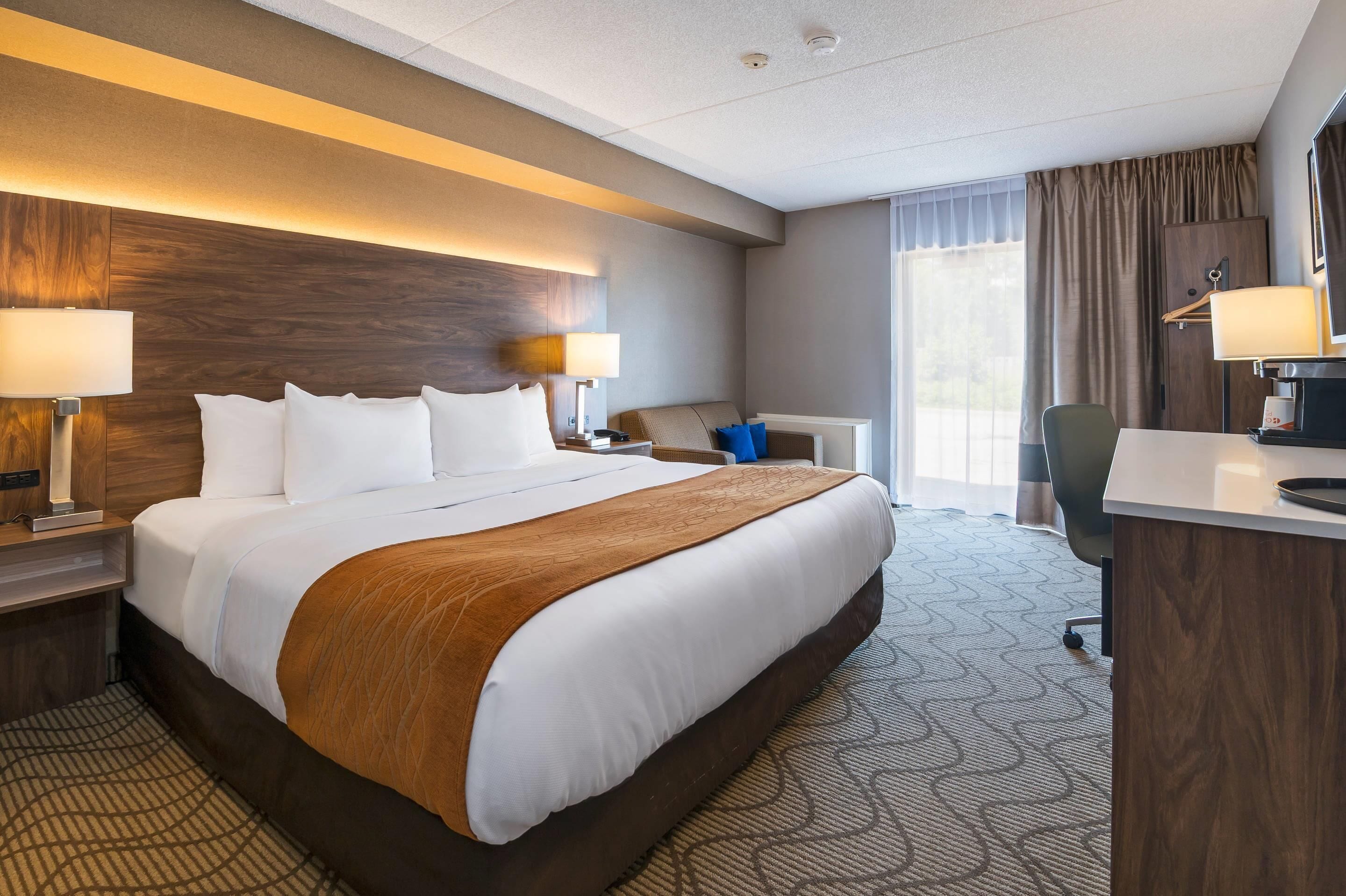 A hotel room with a large bed, bedside lamps, a desk, a chair, and a window with curtains.