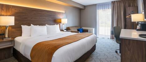 A hotel room with a large bed, bedside lamps, a desk, a chair, and a window with curtains.