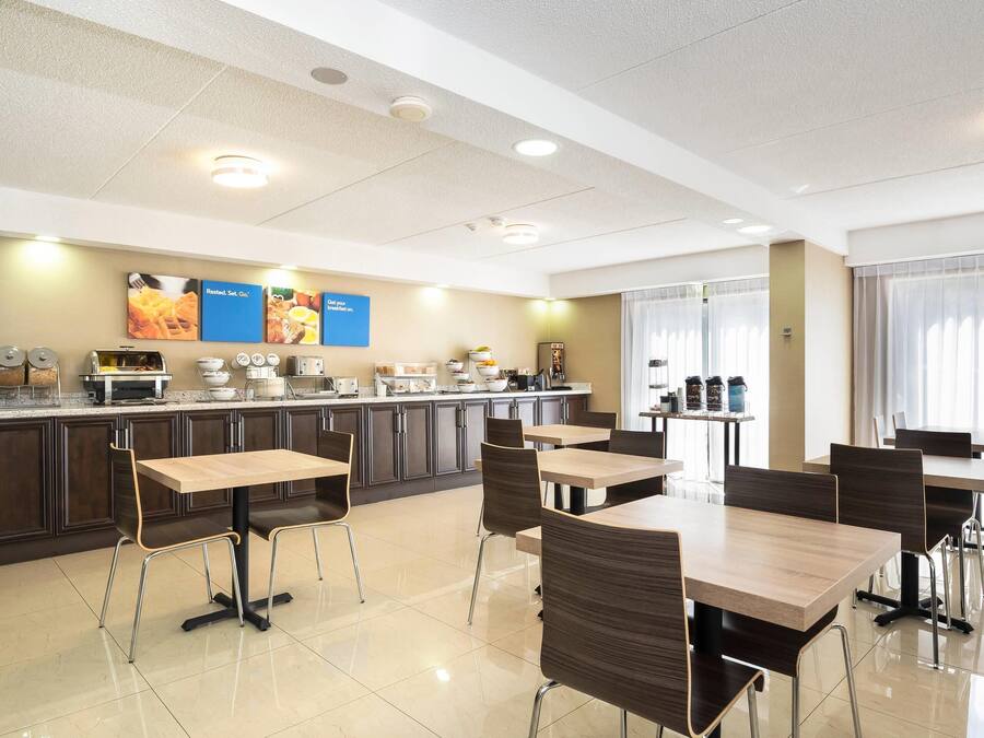 A hotel dining area with a buffet setup, tables, chairs, and a kitchen in the background.