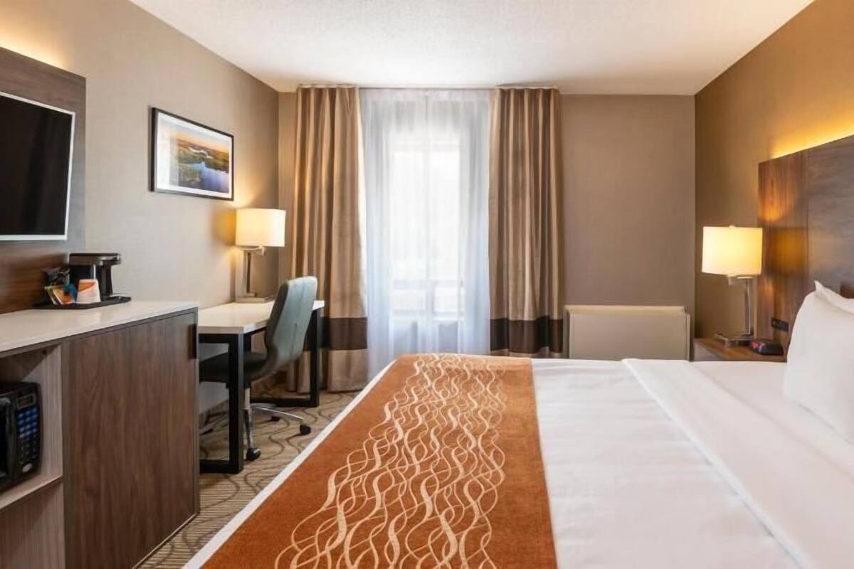 A hotel room with a bed, desk, chair, and a television.