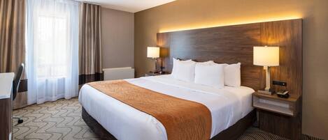 A hotel room with a large bed, two bedside tables with lamps, a desk, and a chair.
