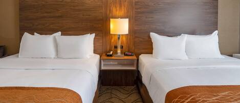 A hotel room with two beds, a nightstand with a lamp, and a patterned rug.