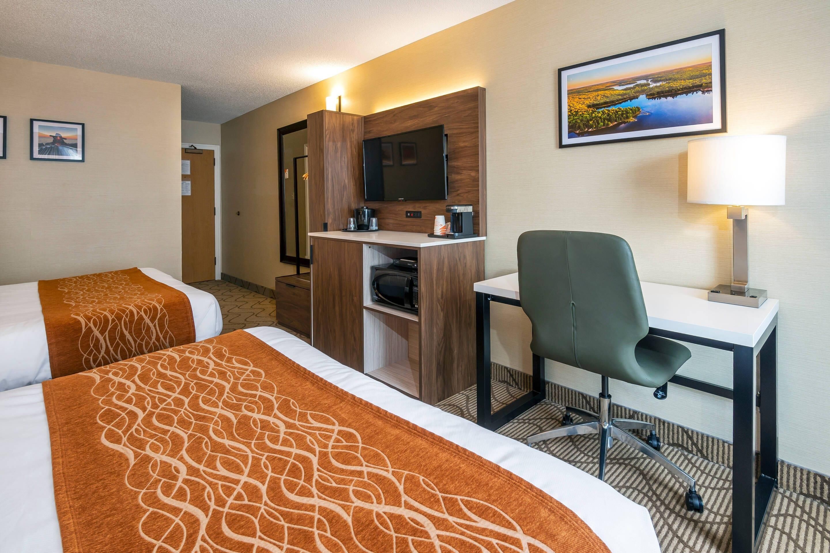 A hotel room with two beds, a desk, a chair, a television, and a painting on the wall.